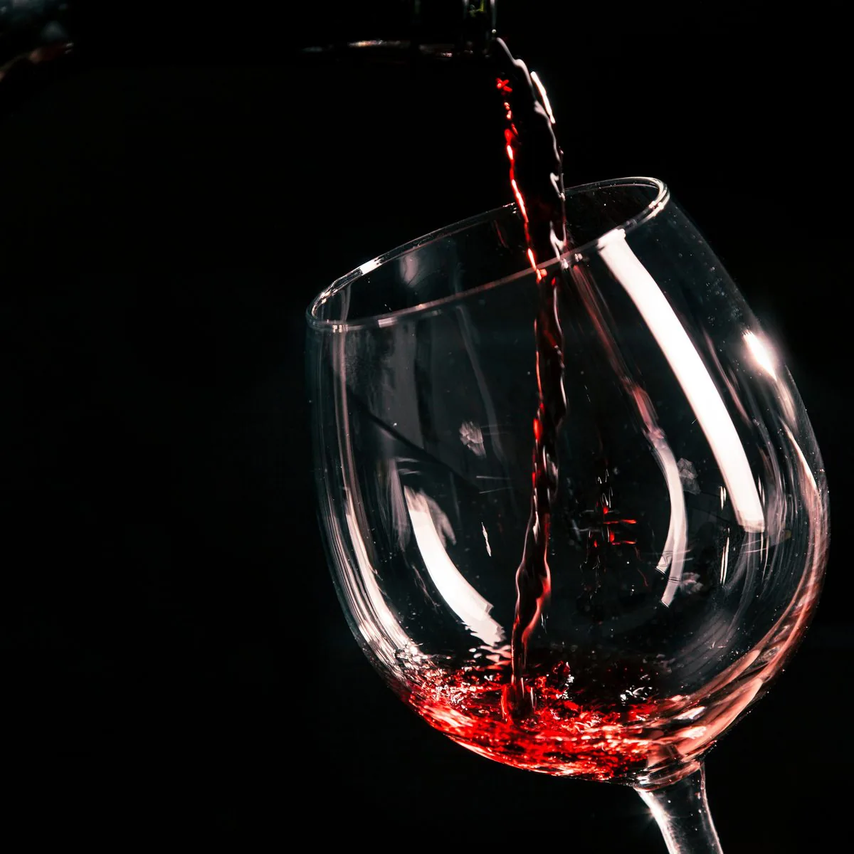Merlot sendo servido em uma taça, sobre fundo escuro.